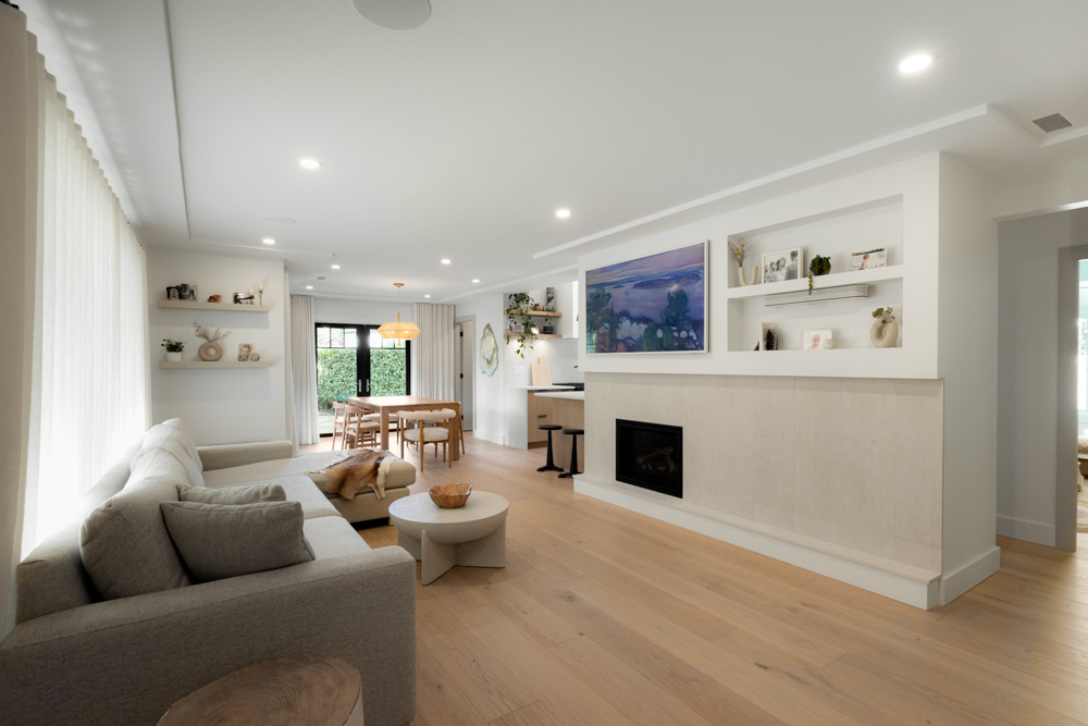 A modern open-concept living and dining area with a neutral color palette, built-in fireplace, and natural wood flooring.