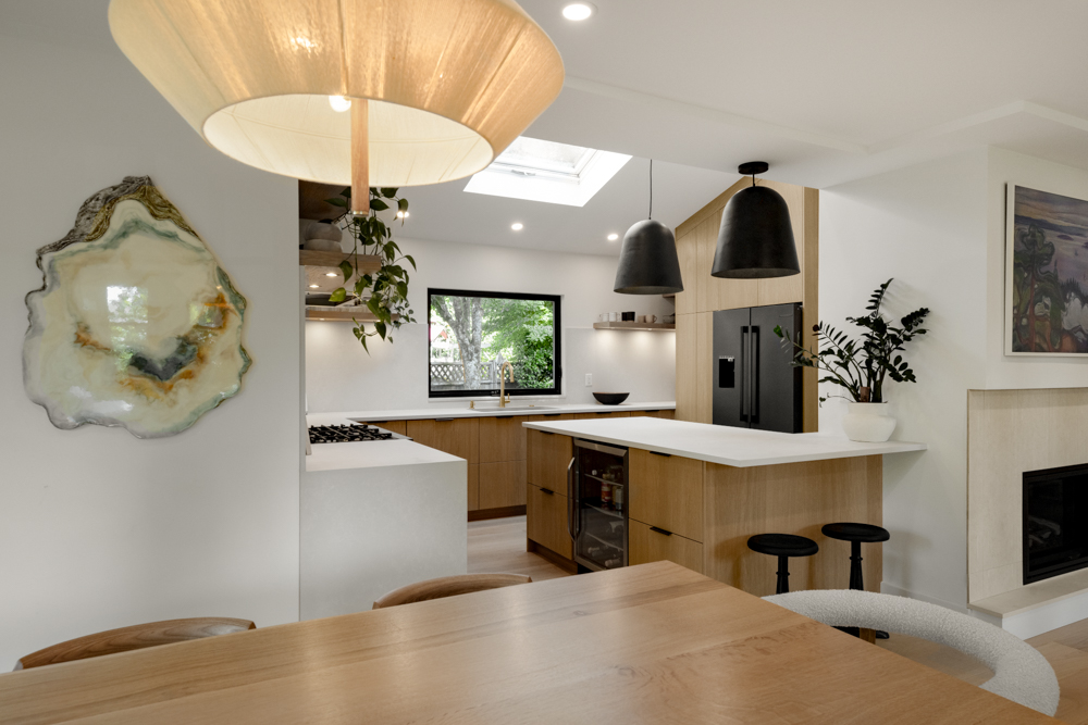 A stylish open-concept kitchen and dining area with natural wood finishes, sleek black accents, and an artistic wall feature.