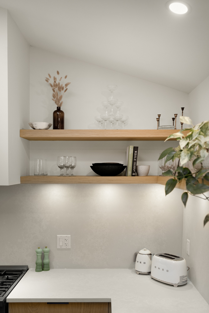 A close-up of a modern kitchen corner featuring open wooden shelves with glassware, ceramics, and decorative accents, complemented by a sleek white countertop and SMEG appliances.