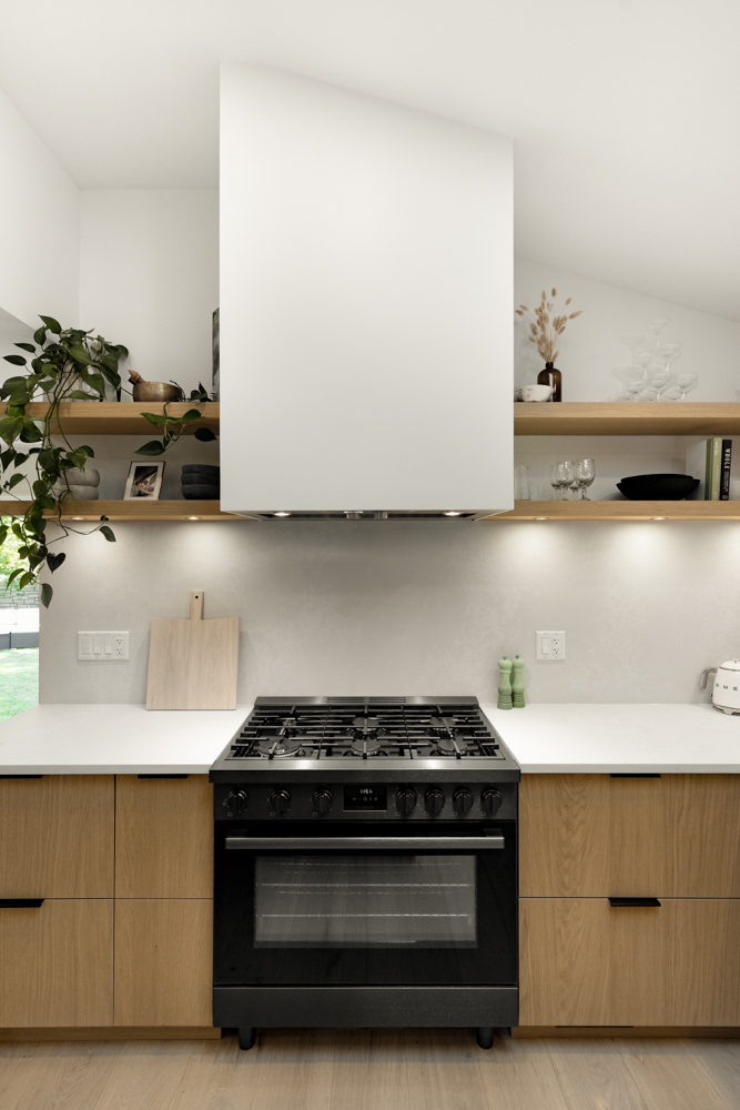 A modern kitchen featuring a sleek black gas range, natural wood cabinetry, and open shelving with curated decor.