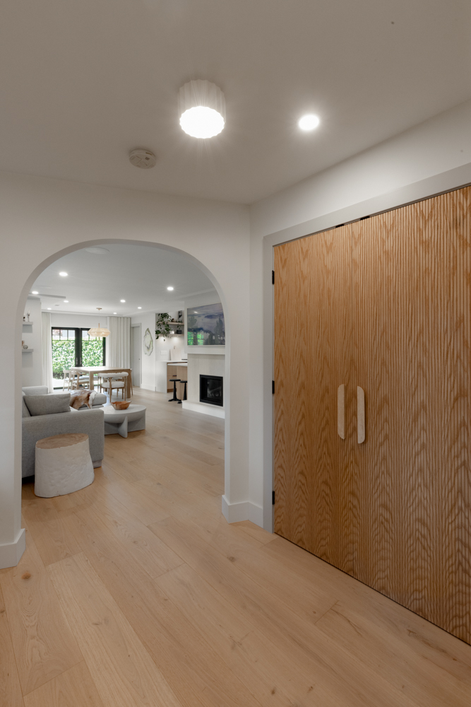 Modern interior hallway featuring light wood flooring, an arched entryway leading to an open-concept living space, and a textured wooden closet door.