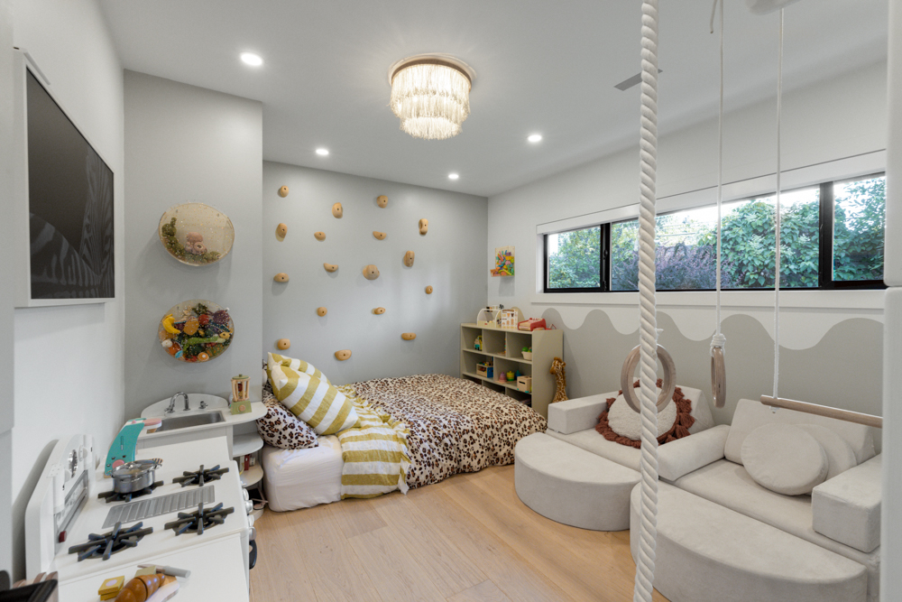 A cozy kids' bedroom with a climbing wall, play kitchen, and soft furnishings in neutral tones.