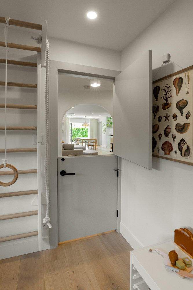 A stylish modern interior featuring a Dutch door, an arched entryway leading to a bright living space, and a wooden climbing structure for kids.