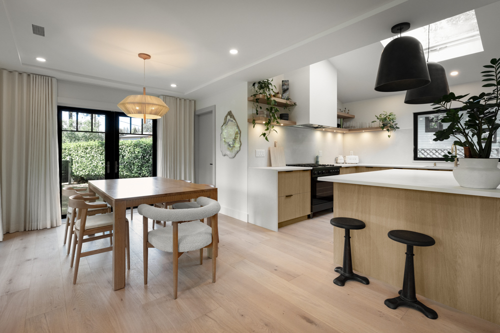 A modern open-concept kitchen and dining area featuring light wood tones, black accents, and natural light.